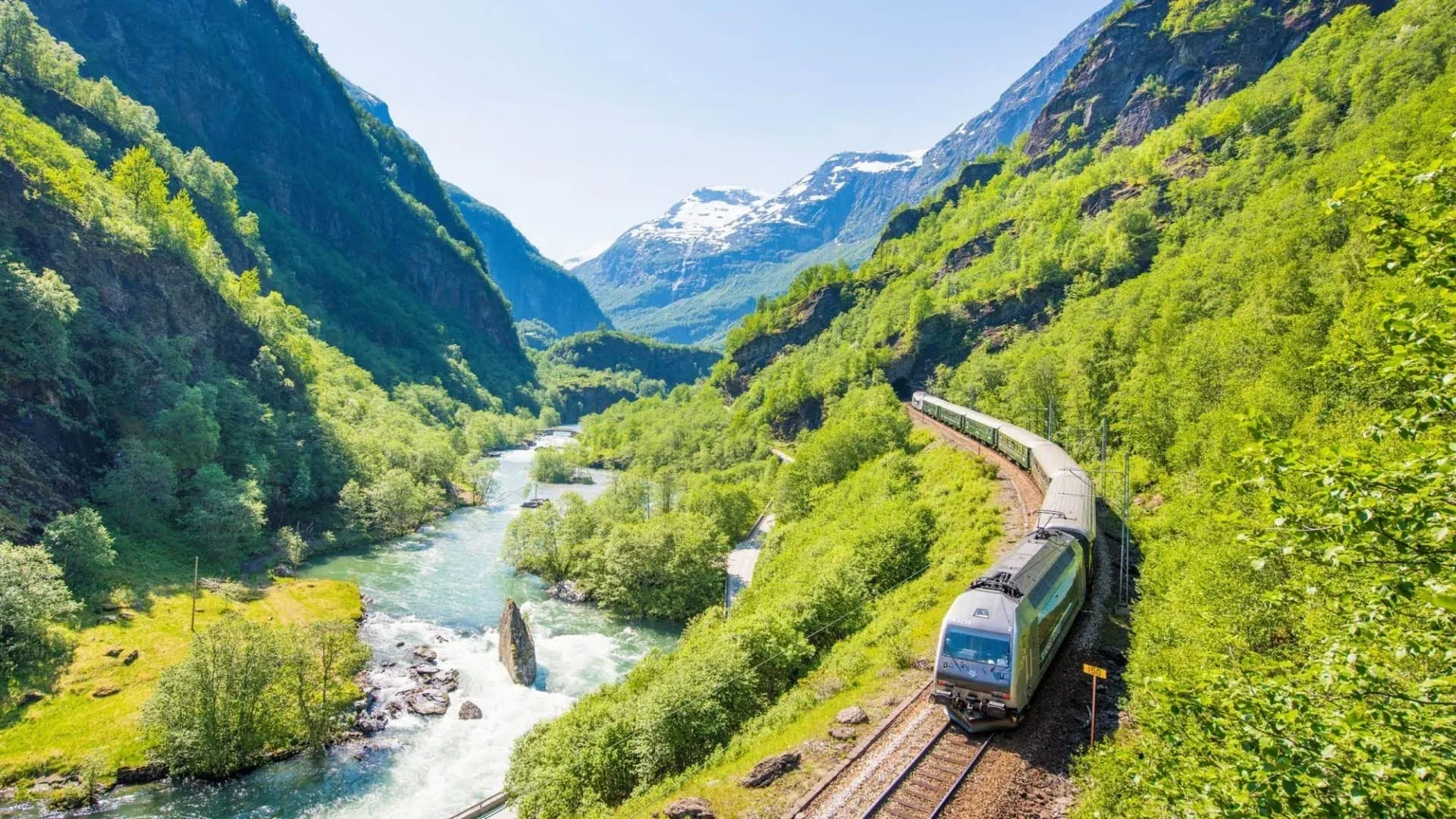 Flåm Railway train following a river through a green mountain valley